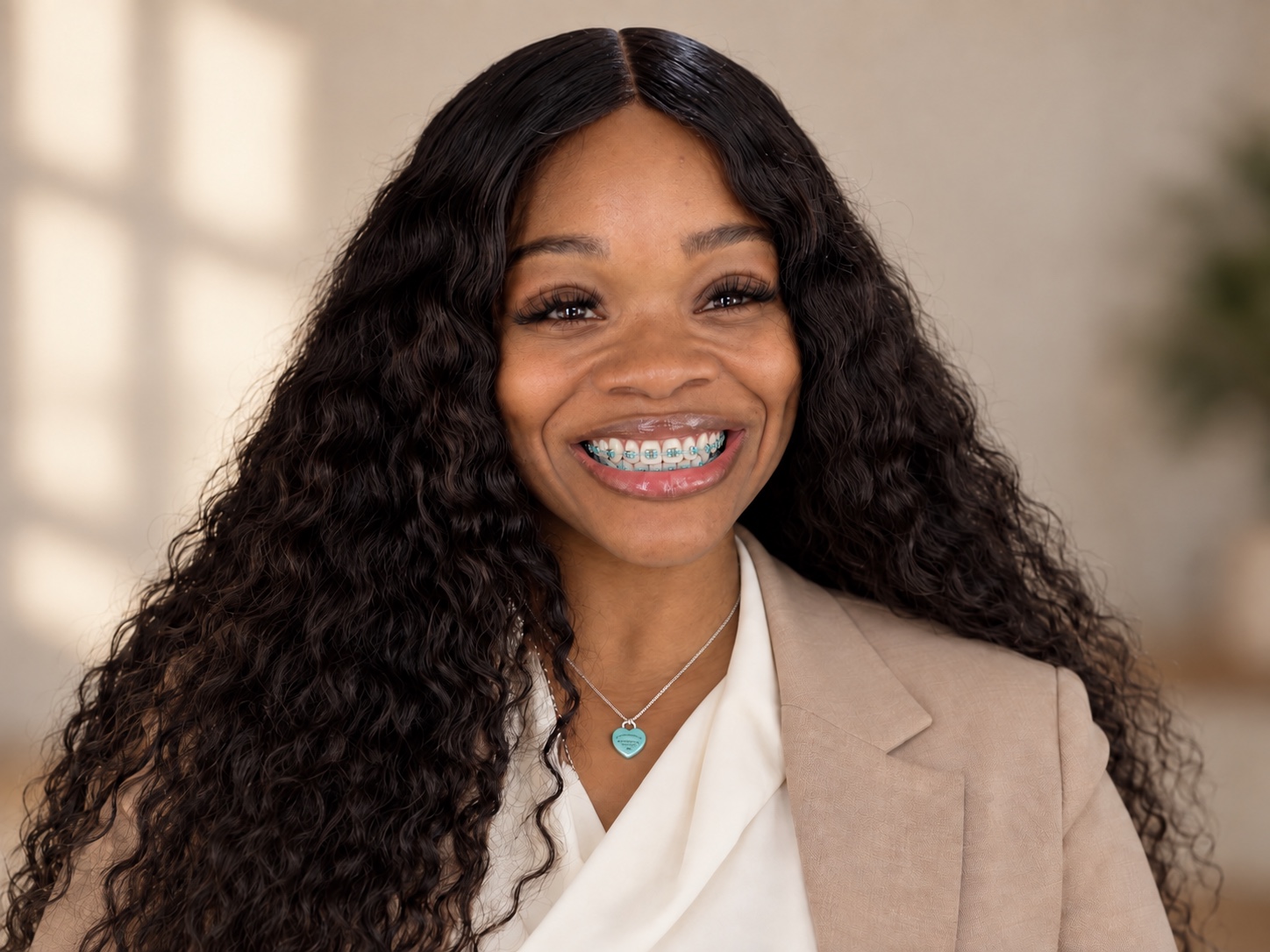Kyra, founder of The Village Nanny Co., smiling in a tan blazer and cream blouse